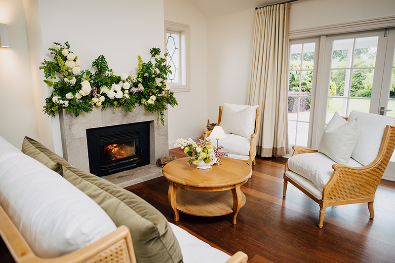 Homestead sitting room with fireplace, floral mantle arrangement, and cane armchairs