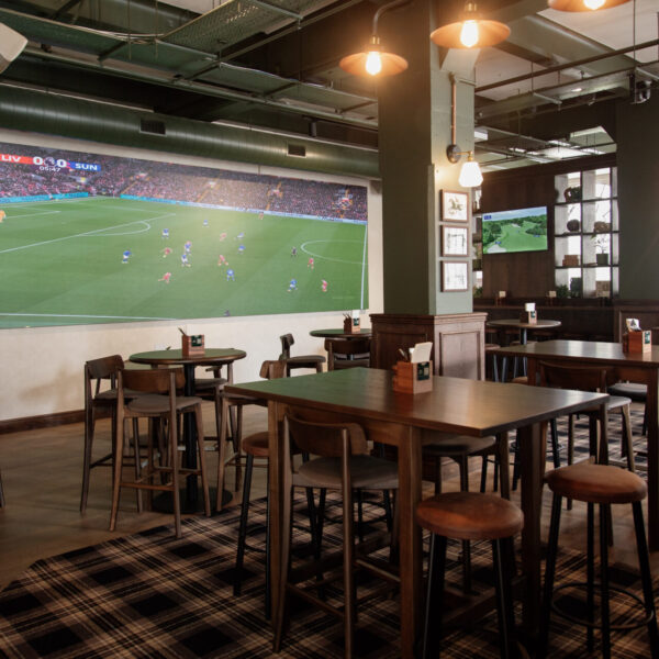 Dark green bar interior with large screen, plaid carpet, and high wooden tables