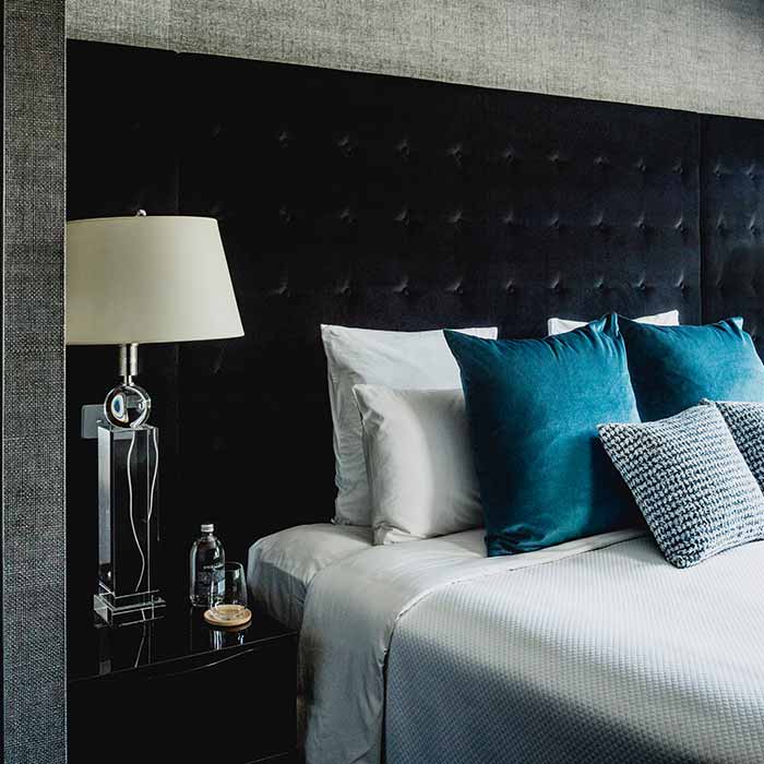 Hotel room with dark tufted headboard, teal cushions, and bedside lamp