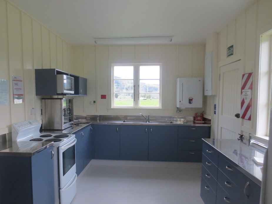 Functional hall kitchen with blue cabinetry, stainless bench and sink, electric stove, and garden window