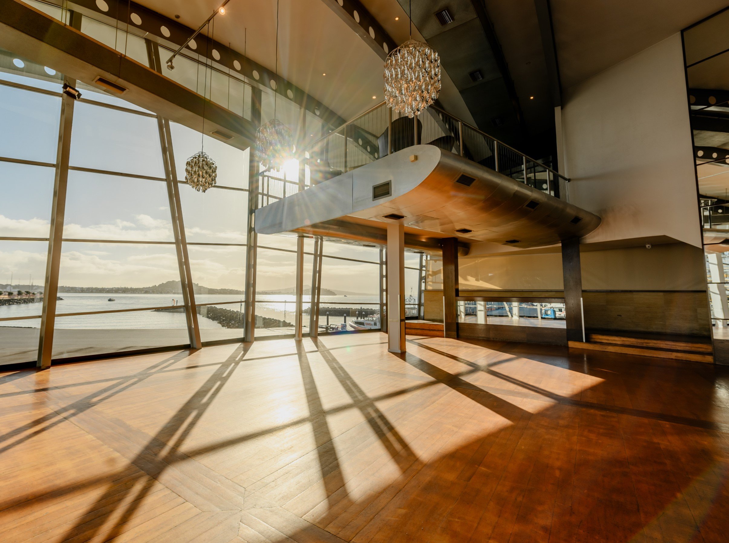 Curved steel and timber interior with large windows overlooking a waterway, suspended mezzanine and pendant lights
