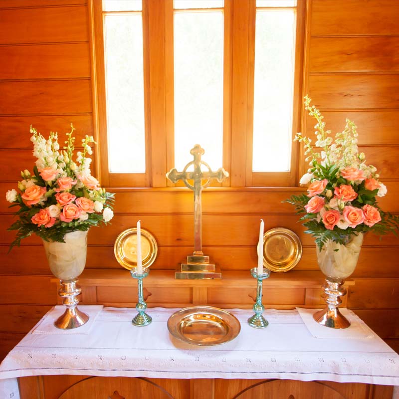 Church altar with cross, candles and flower arrangements on timber panelled walls