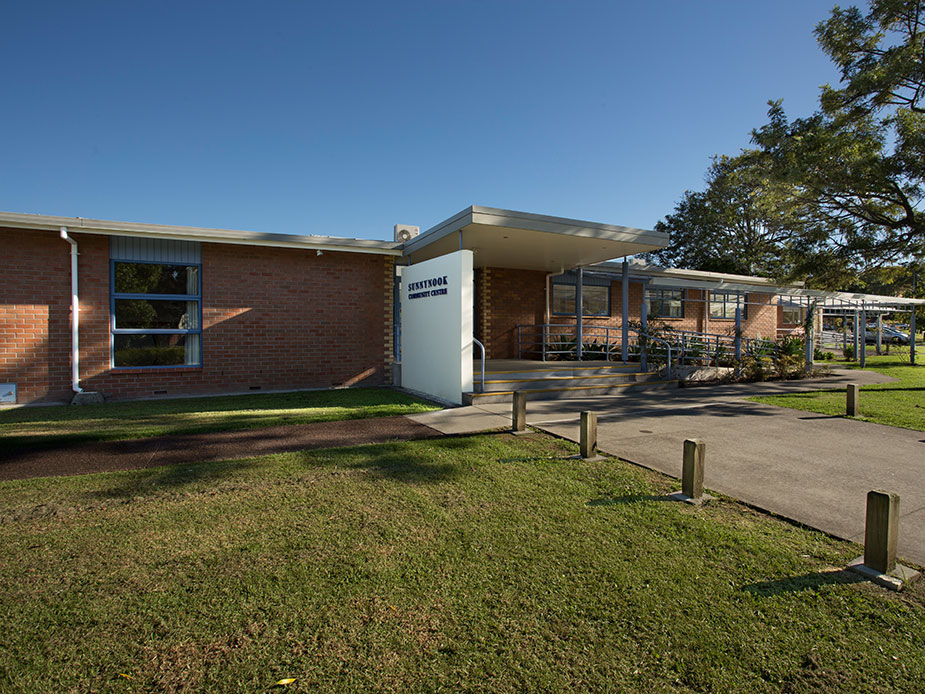 Low-rise brick community centre building with covered entrance and lawn