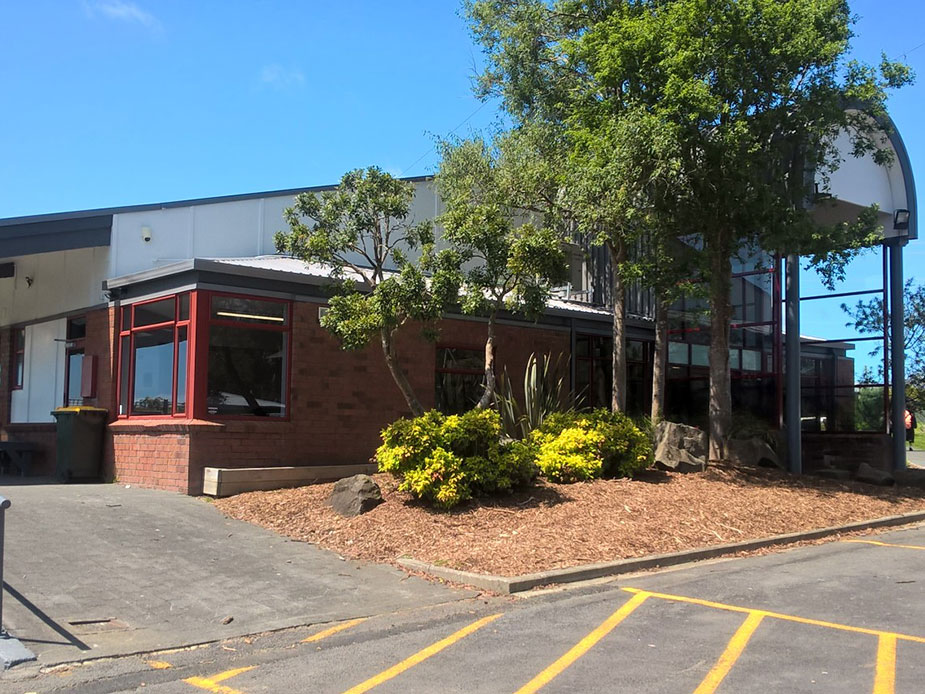 Community hub building with brick and metal cladding, trees, and garden border