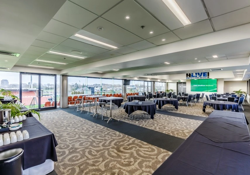 Stadium lounge set up for a conference with round tables and a large screen