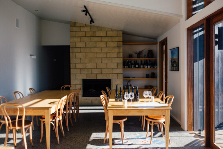 Timber-tabled meeting room with bentwood chairs, stone fireplace, and wine bottles on shelves