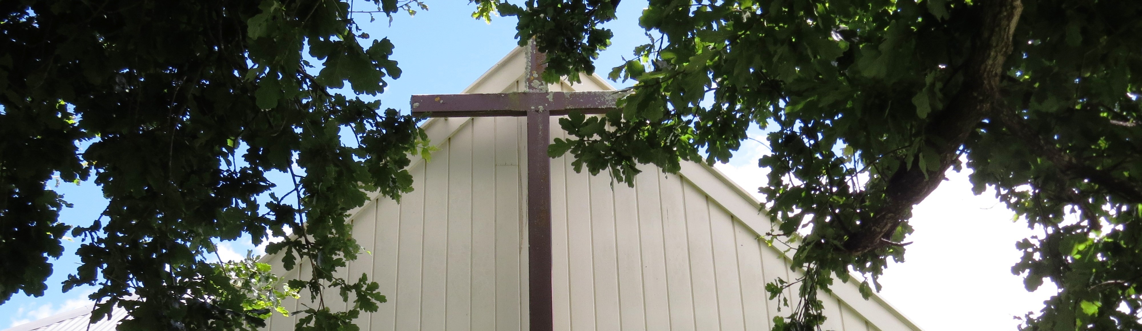 Church cross and white timber wall framed by tree canopy