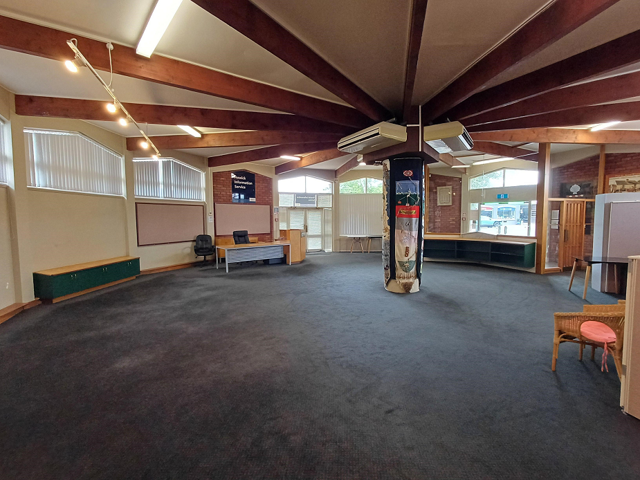 Large open room with timber beam ceiling, carpet, central decorative column and information displays