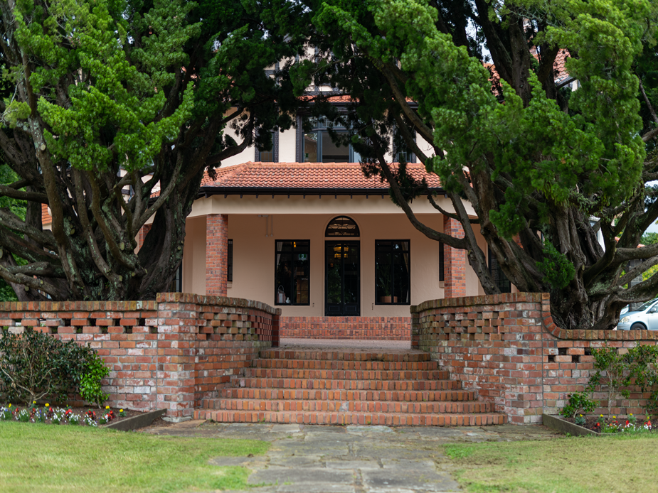 Cream render homestead front entrance with red brick steps, arched gate, and large trees either side
