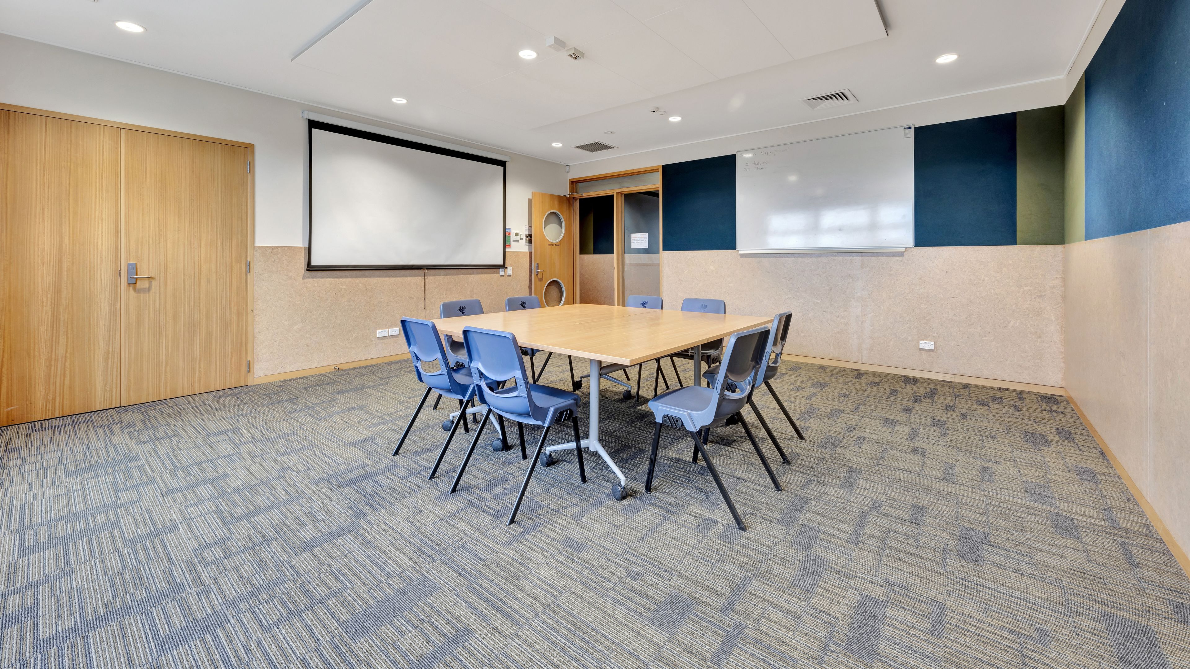 Meeting room with small table, blue chairs, projection screen and whiteboard
