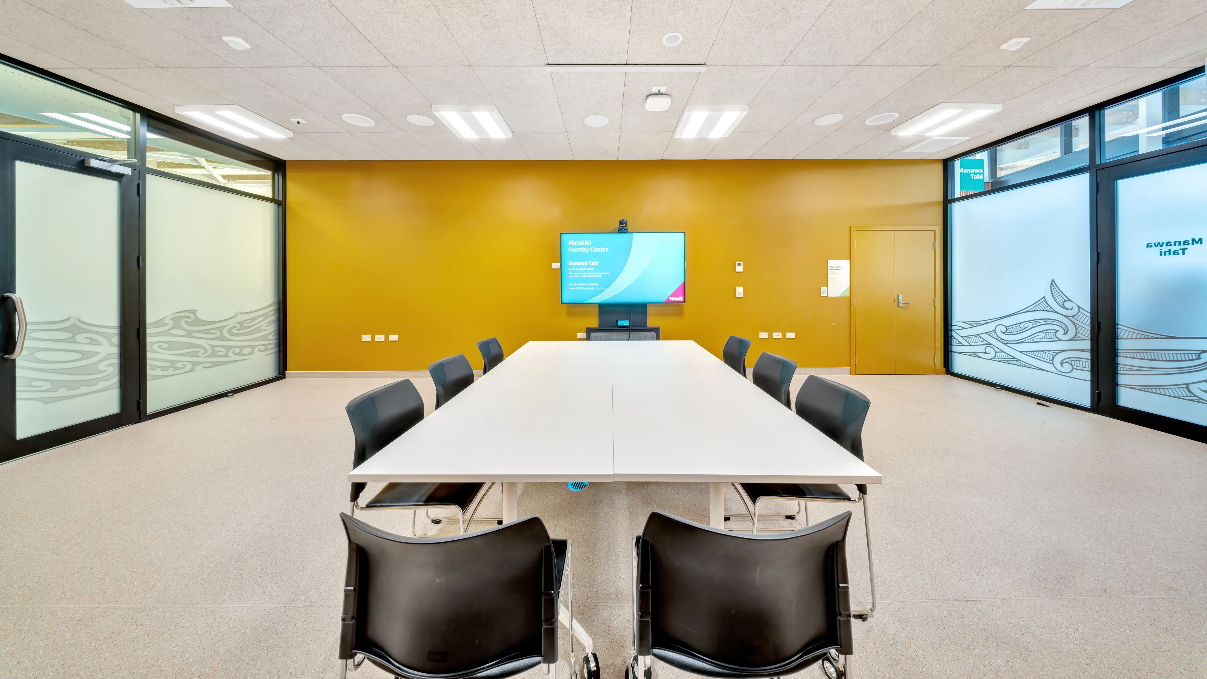 Boardroom with white table, chairs and wall-mounted screen on yellow wall