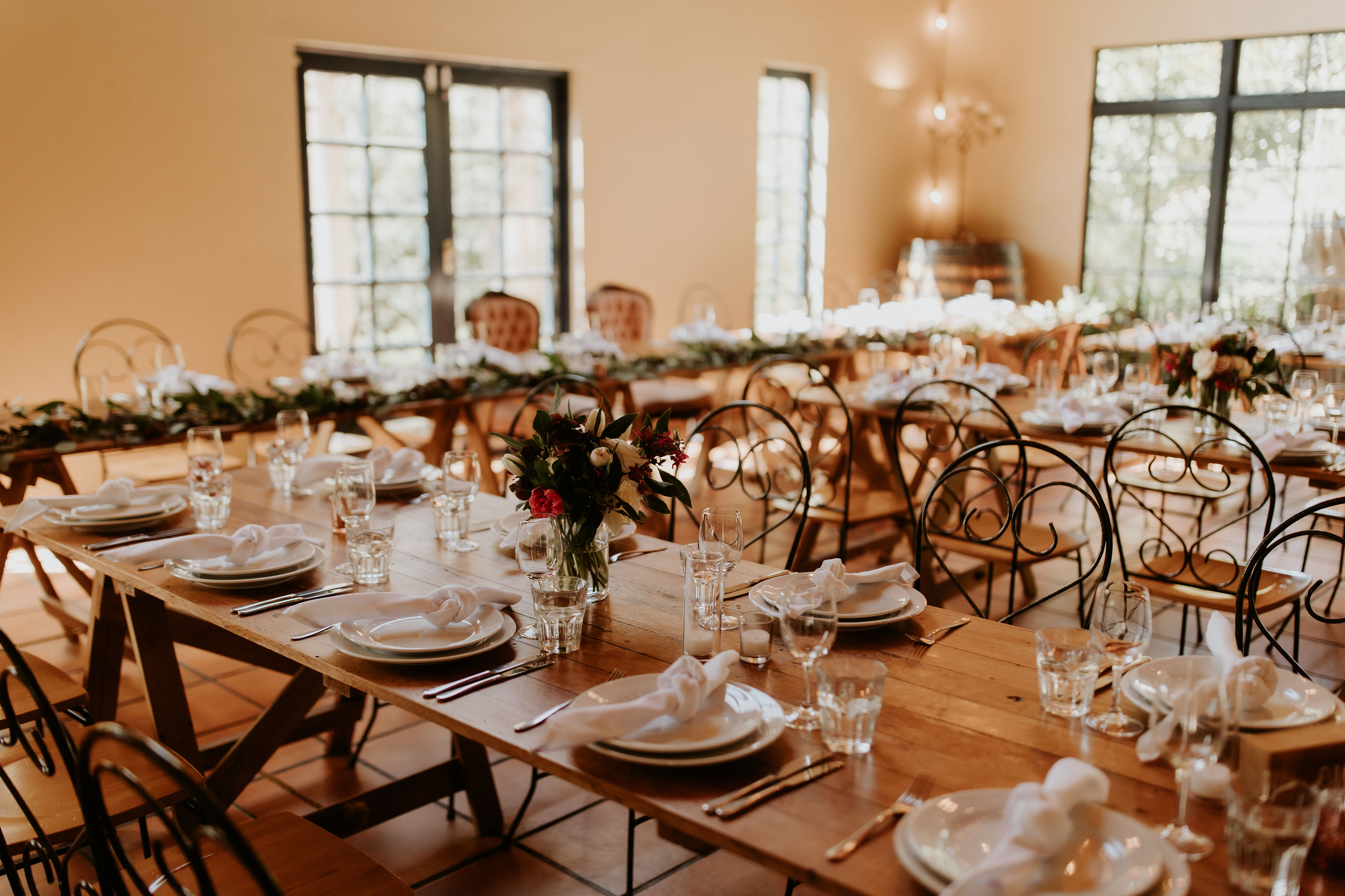 Timber trestle tables set for a reception with iron chairs and large steel-framed windows