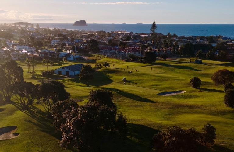 Aerial view of golf course with coastal town and ocean in background