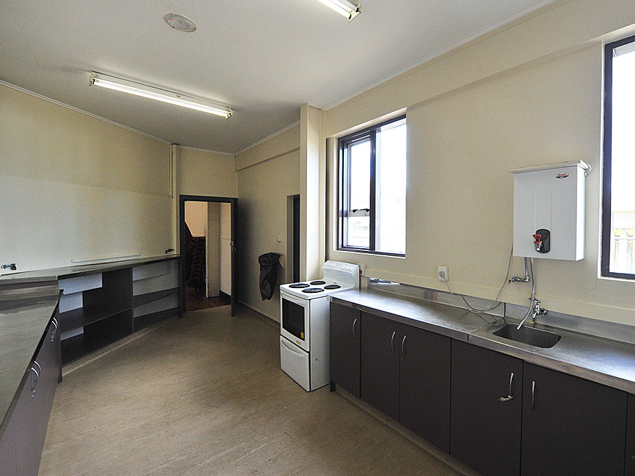Plain community kitchen with dark cabinets, electric stove, and stainless bench