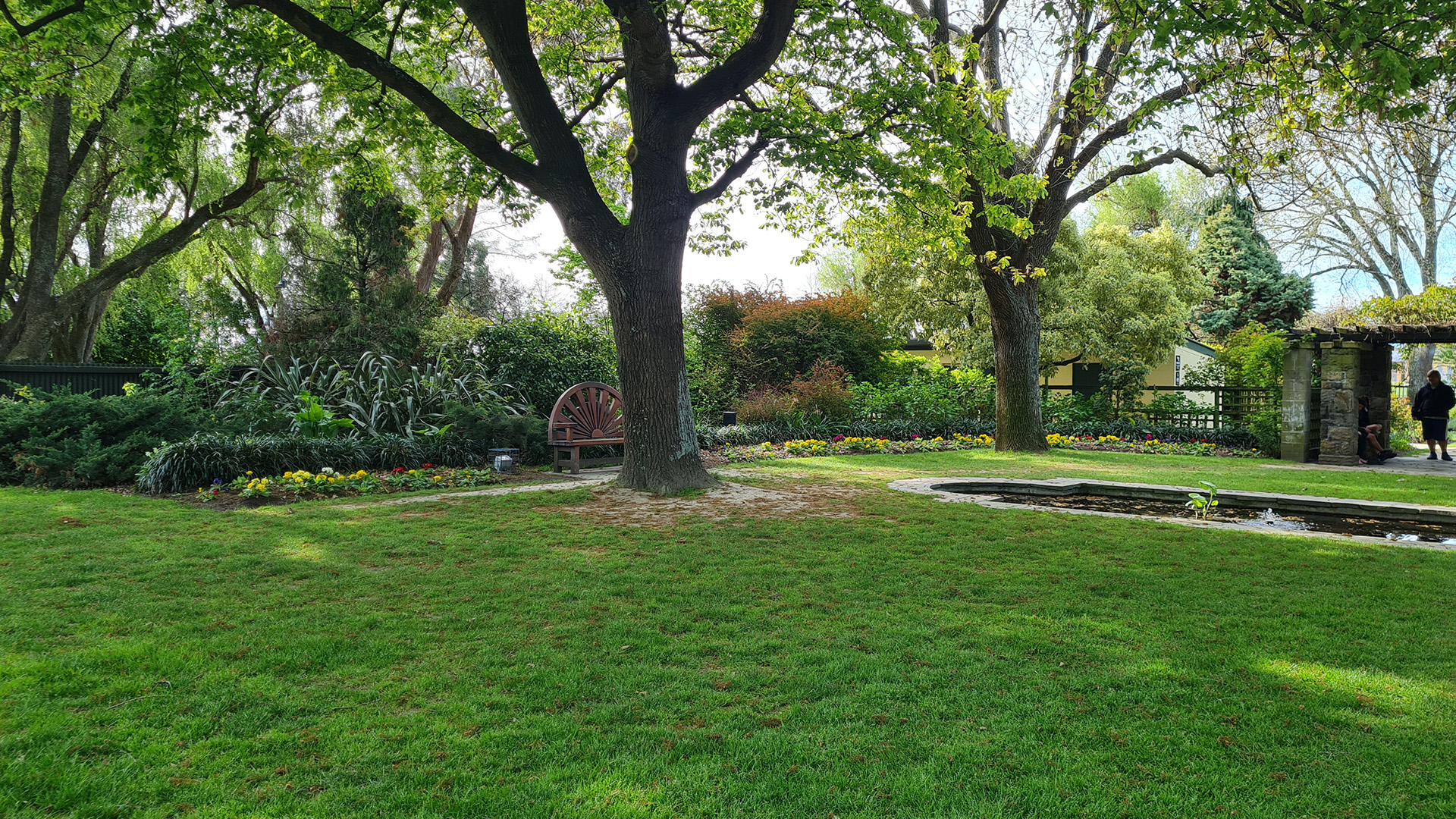 Landscaped garden with lawn, mature trees, bench and water feature