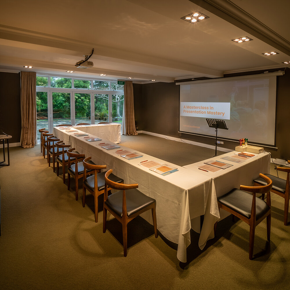 Meeting room set in U-shape with timber chairs, projection screen, and garden window