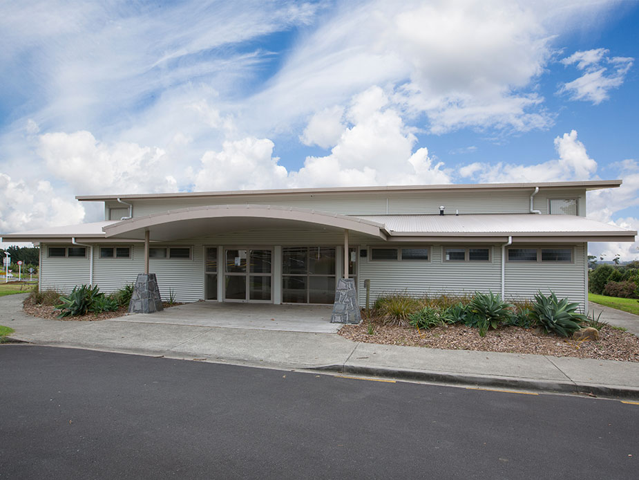 Single-storey hall with curved roof canopy, corrugated cladding and planted entrance