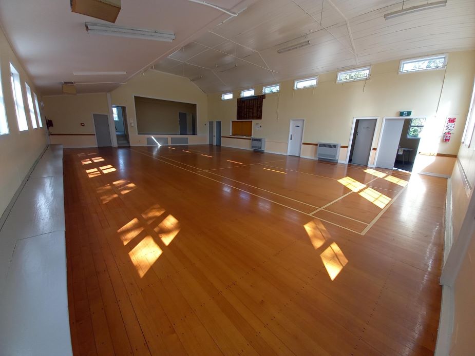 Wide empty hall with polished timber floor and elevated platform at the far end