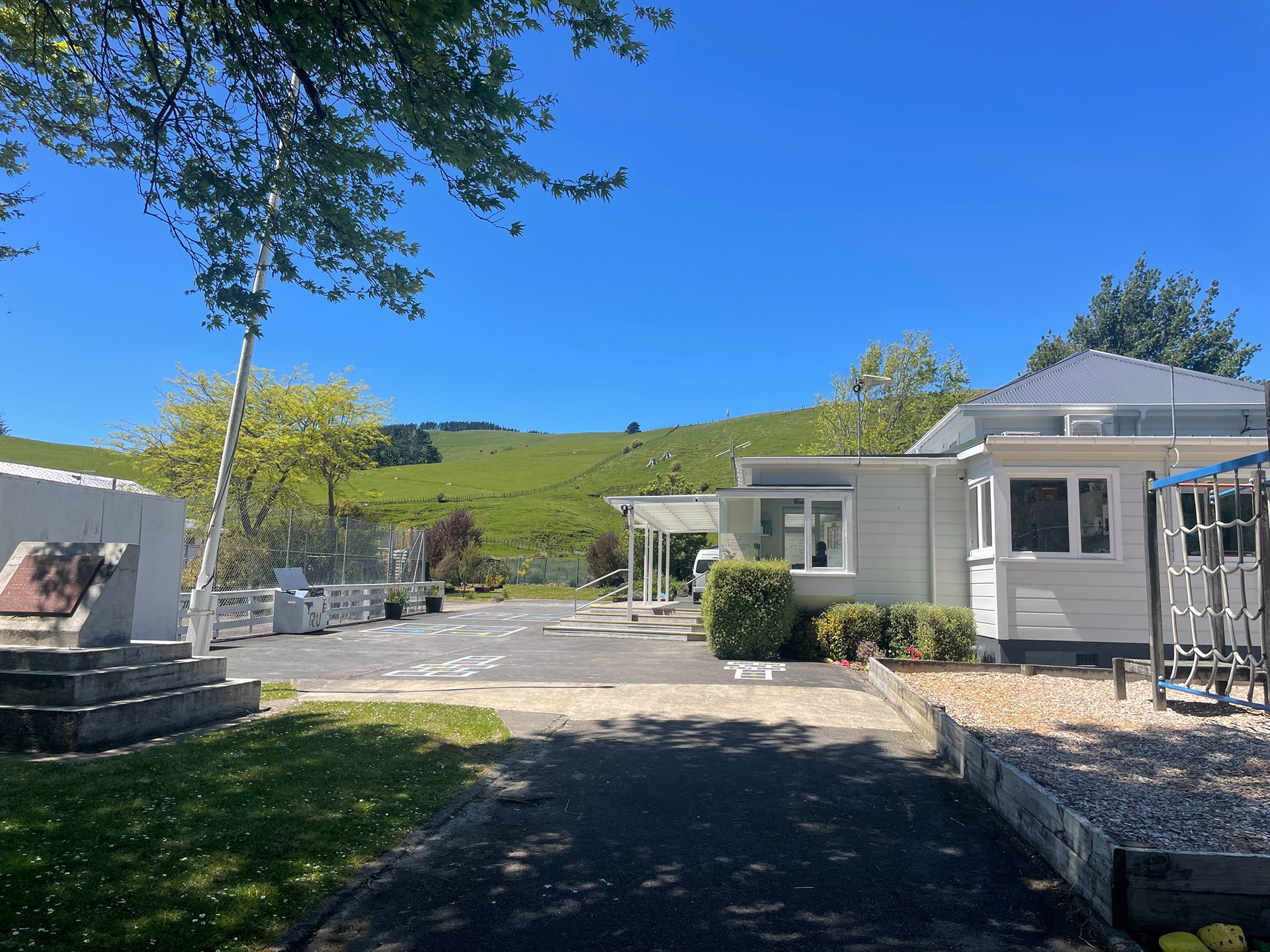 White hall building with playground and rolling green hills behind