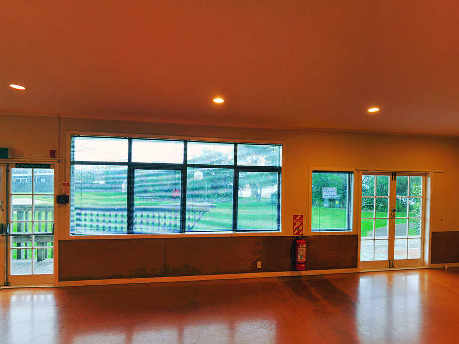 Empty hall room with timber floor and large windows overlooking outside green space