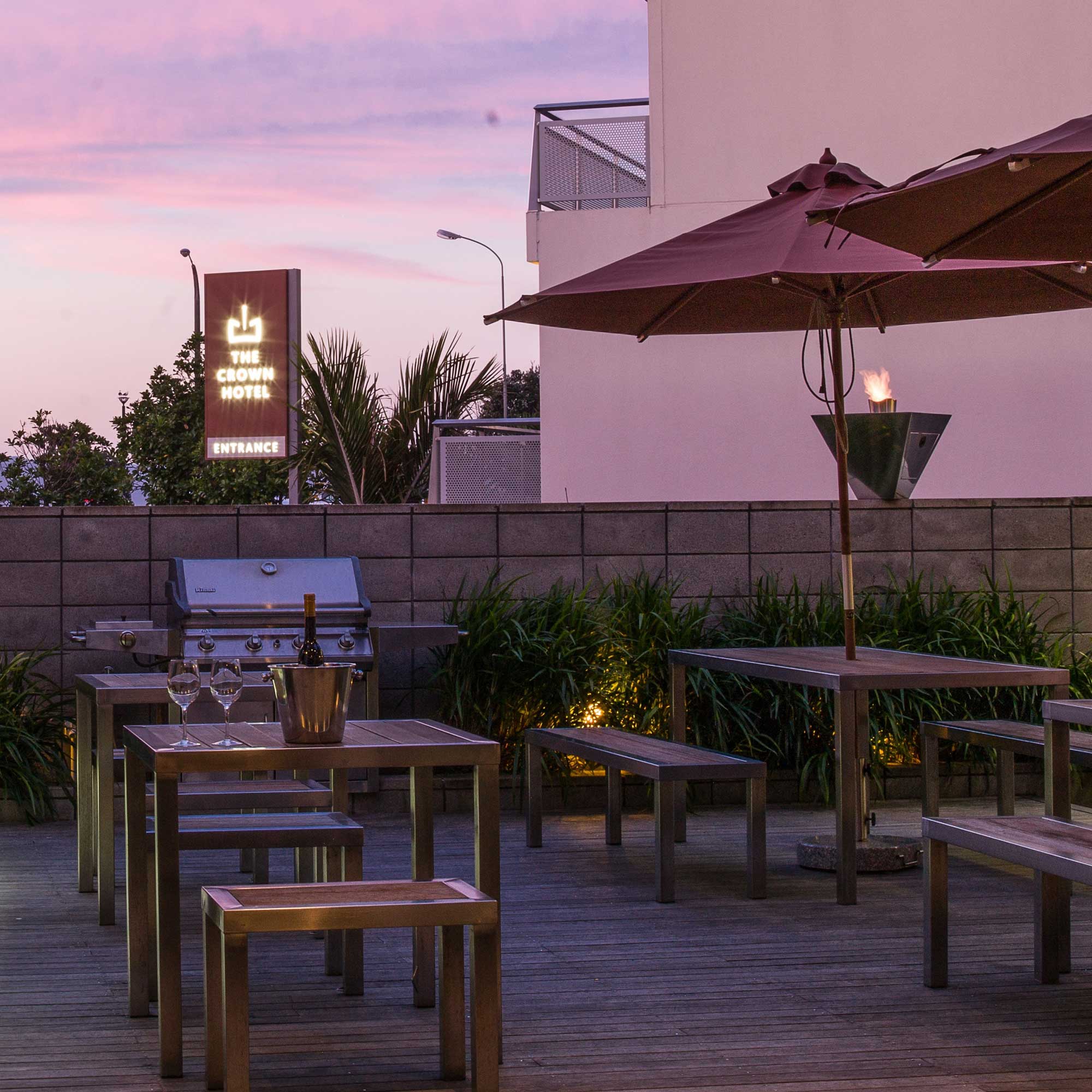 Rooftop terrace at dusk with timber tables, market umbrella, gas torch, garden strip