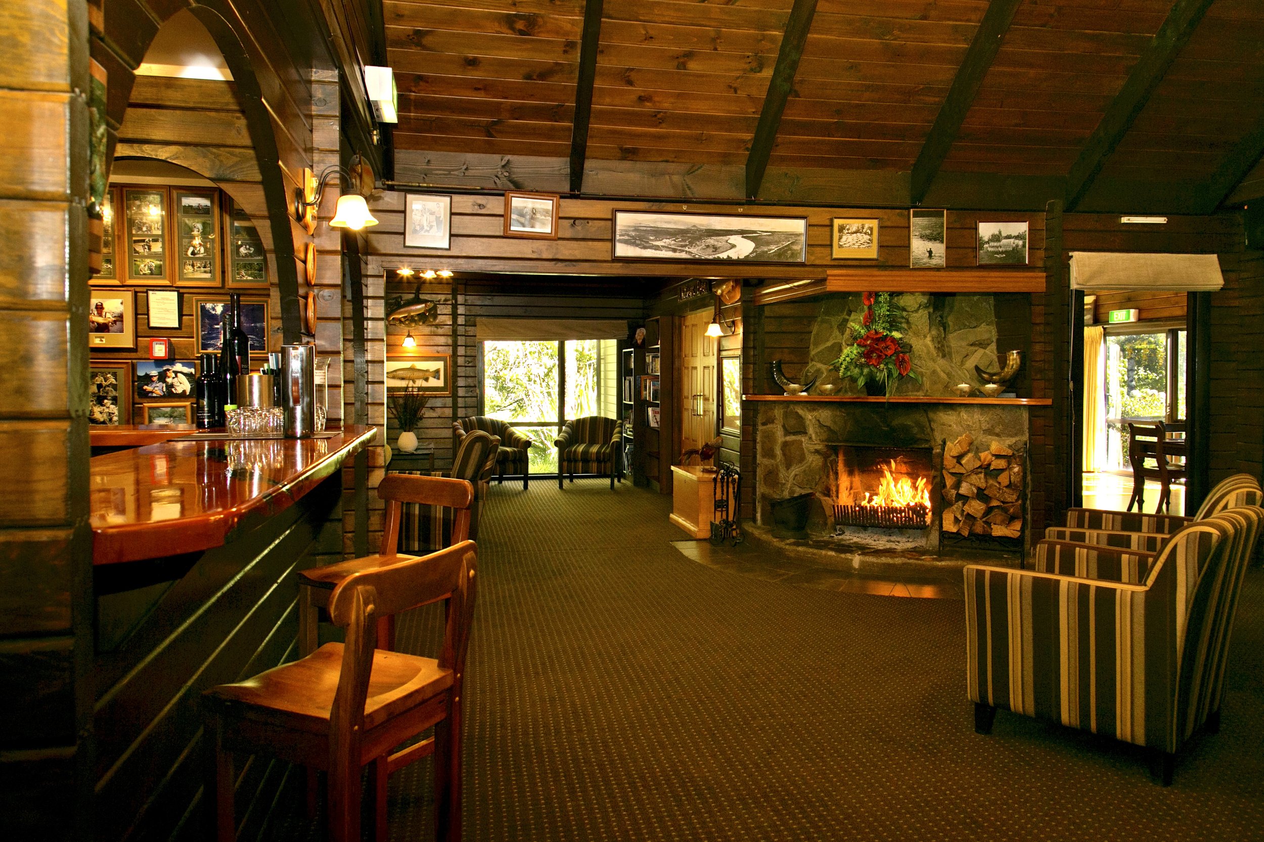 Timber-lined lodge bar and lounge with stone fireplace, framed artworks, and wood bar counter