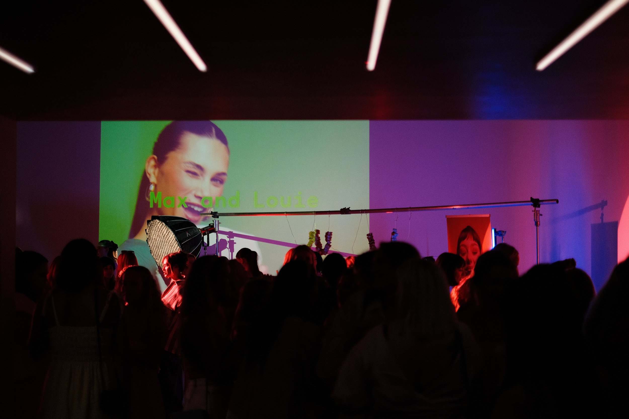 Event space with coloured projection lighting, screen, crowd, and microphone stand