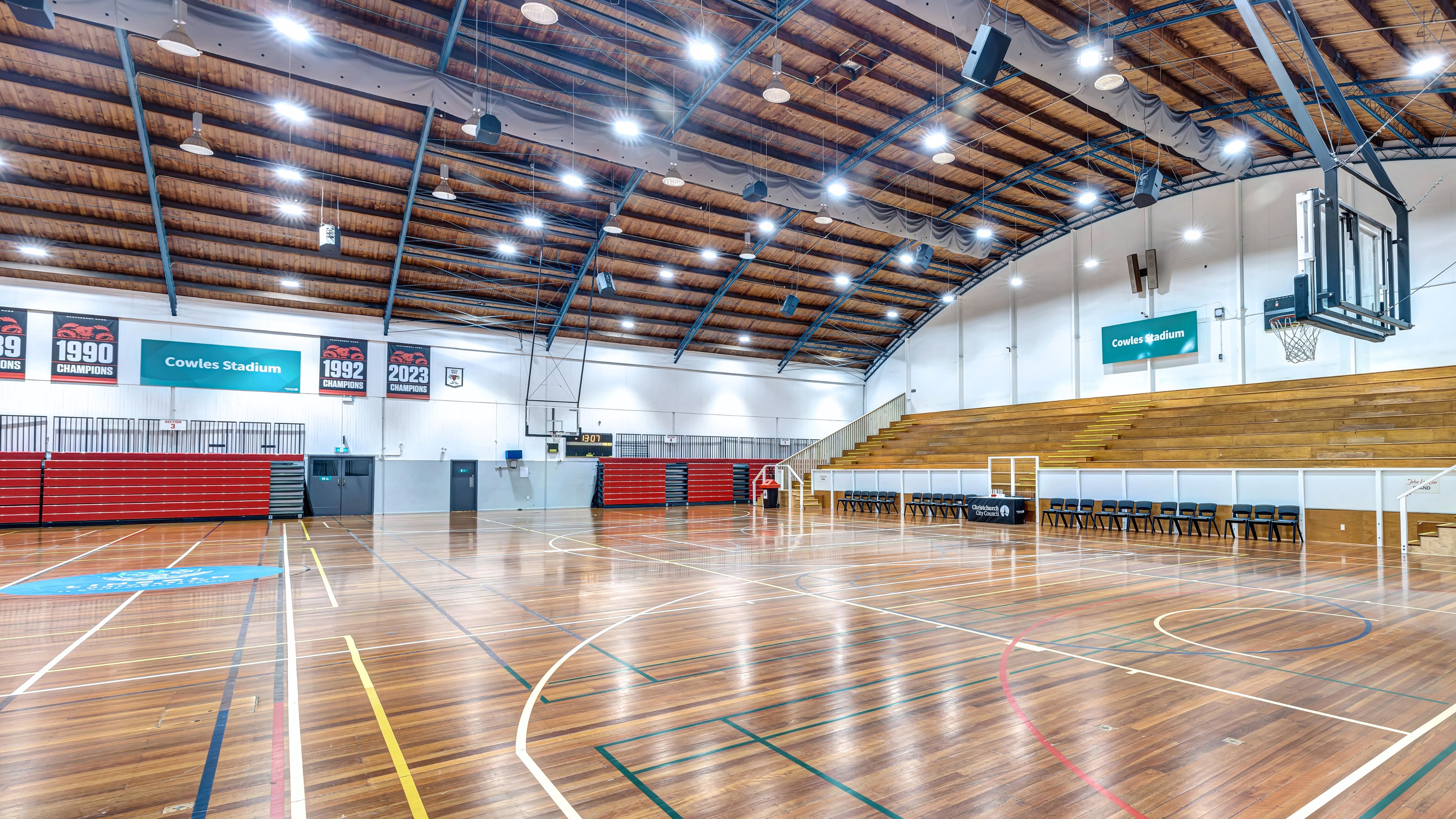 Large indoor stadium with timber floor, tiered seating, and banner signs