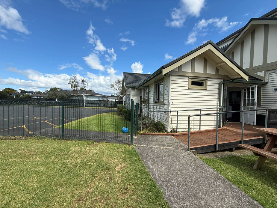 White timber community house side view with ramp, deck and fence