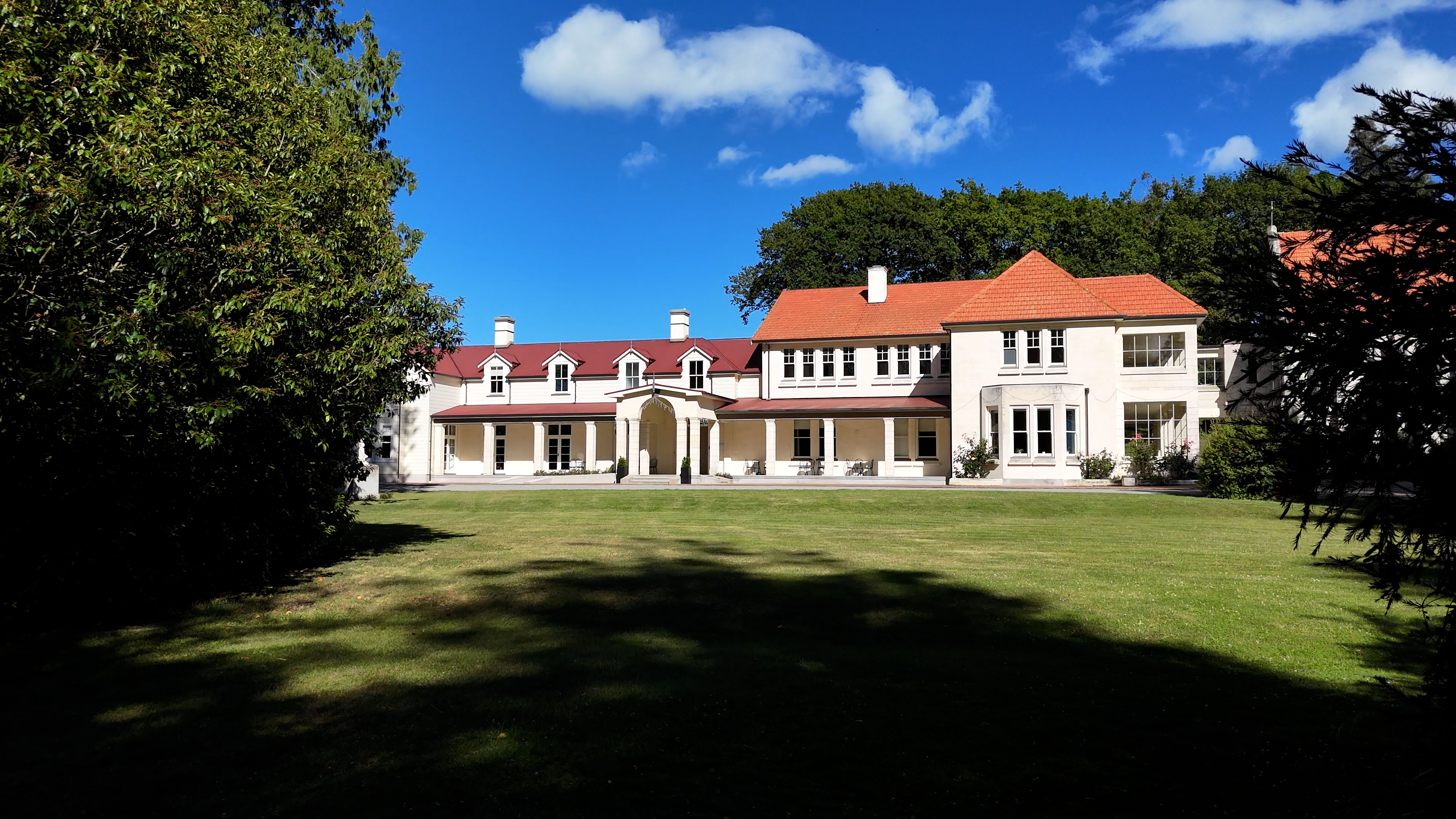 Large white rendered mansion with terracotta tile roof, columned portico, sweeping lawn