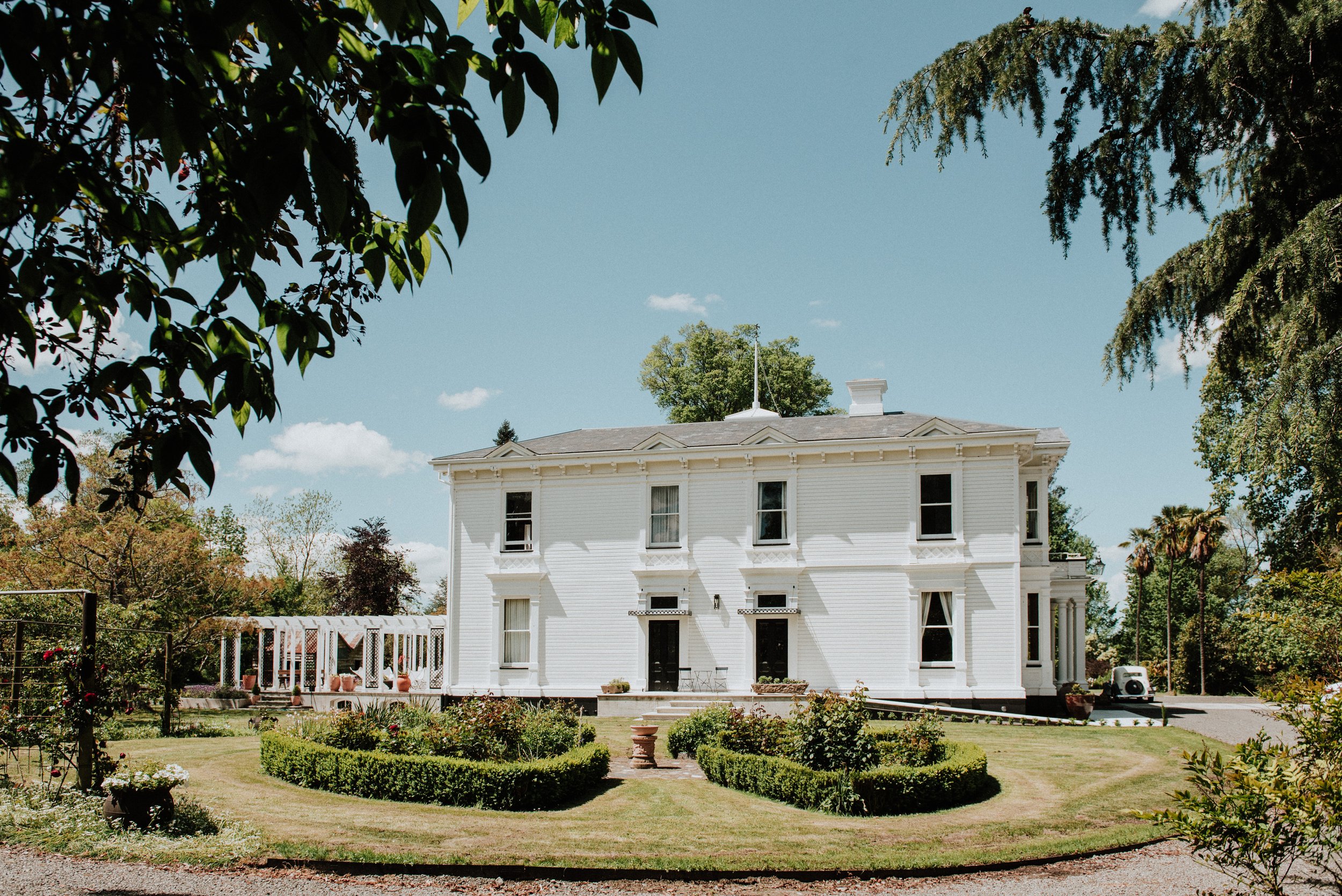 White two-storey villa with formal garden and pergola in foreground