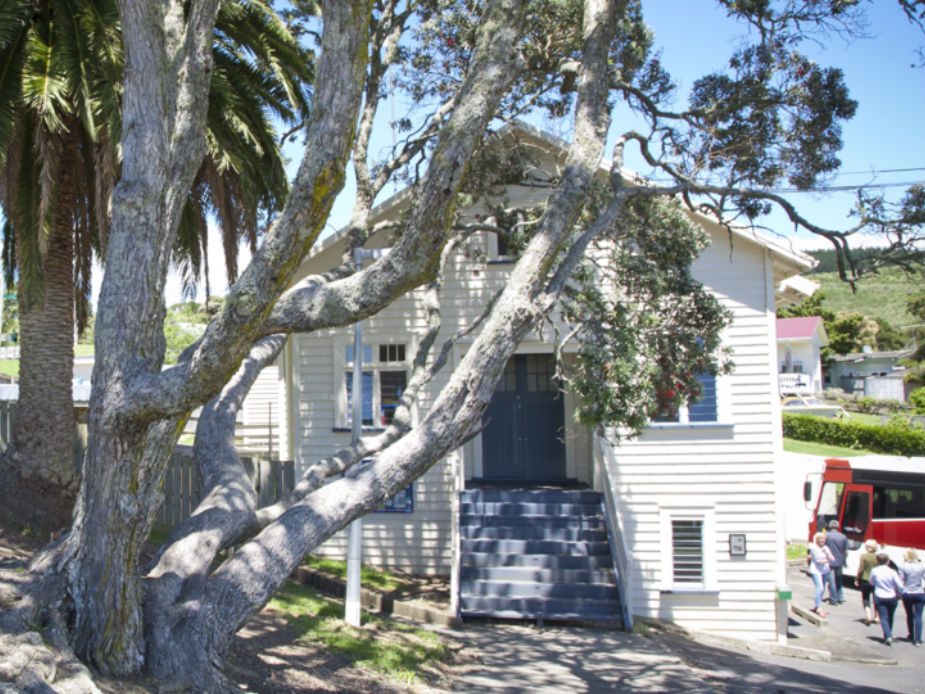 White weatherboard hall with large trees framing the entrance and steps