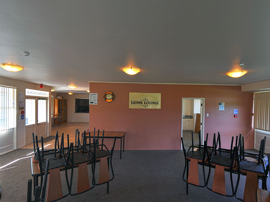 Hall interior with stacked chairs and tables, Lions Lounge sign on pink wall