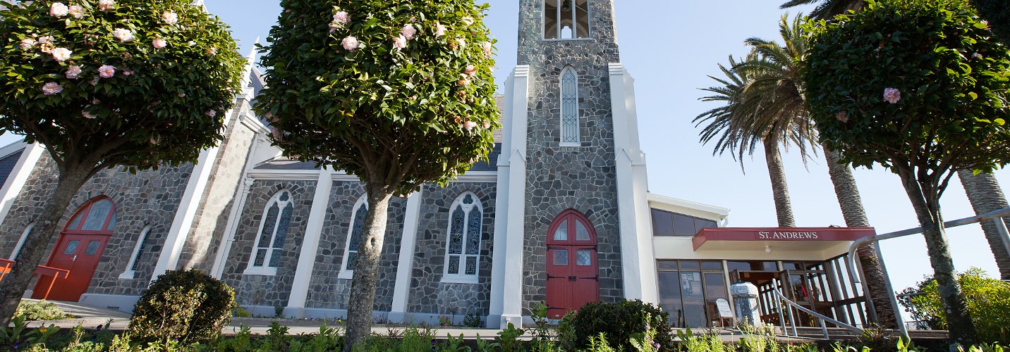 Dark stone church with tall bell tower, red arched doors, and trees lining the path