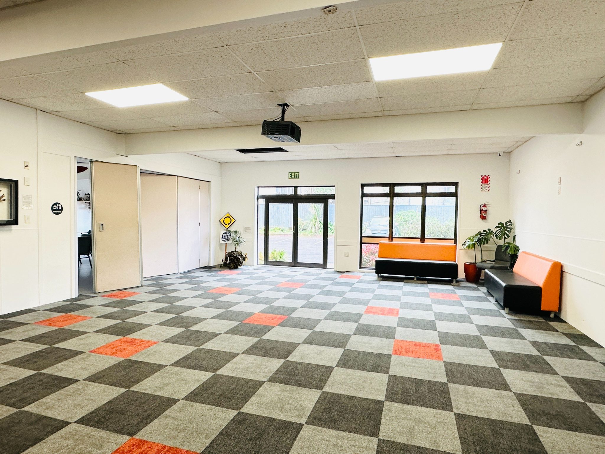 Open multipurpose hall with chequered carpet, projector and orange lounge seating