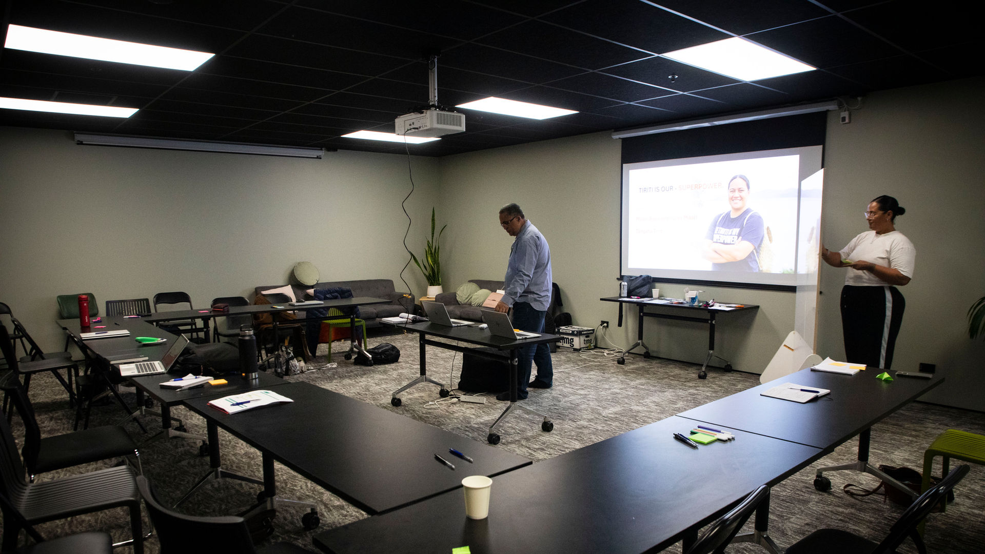 Meeting room with tables, chairs and projector screen showing presentation