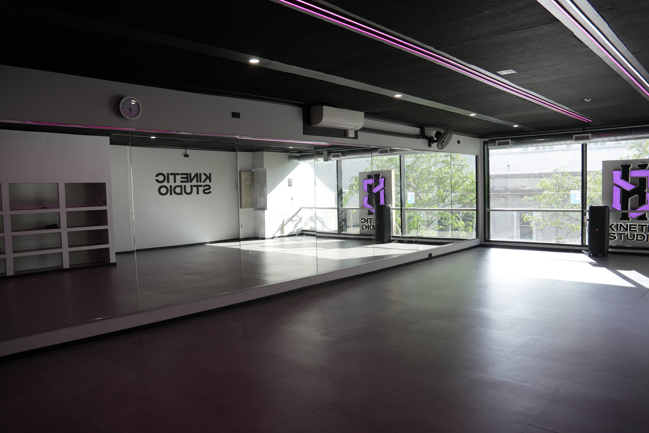 Dark-ceilinged studio with a mirrored wall, vinyl floor, and large street-facing windows