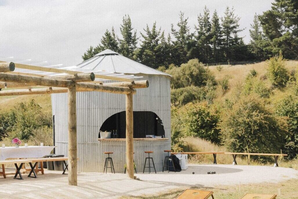 Corrugated iron cylindrical bar structure with open serving arch and timber-log pergola beside it