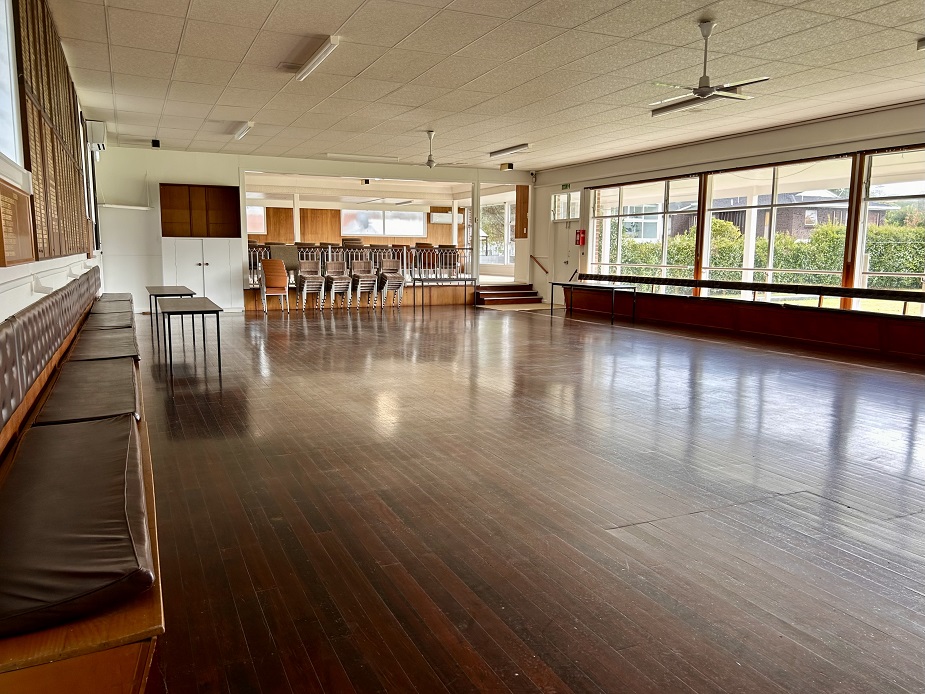 Large open hall with polished timber floors, ceiling fans and stacked chairs