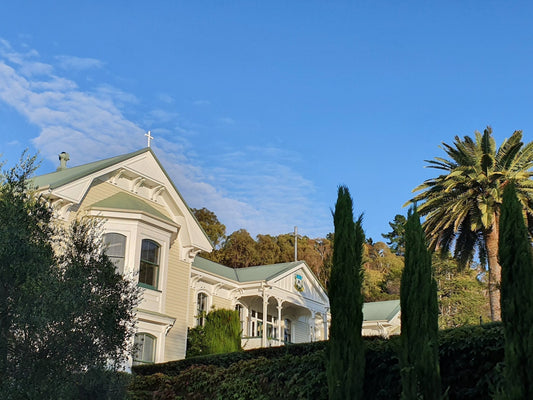 Heritage villa exterior with cross-topped gable, palm trees and gardens