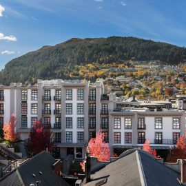 Multi-storey pale hotel building viewed from above with a tree-lined town and hillside behind