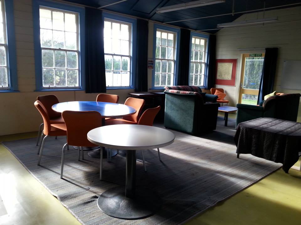 Casual lounge room with round tables, mixed chairs and bright windows with blue trim