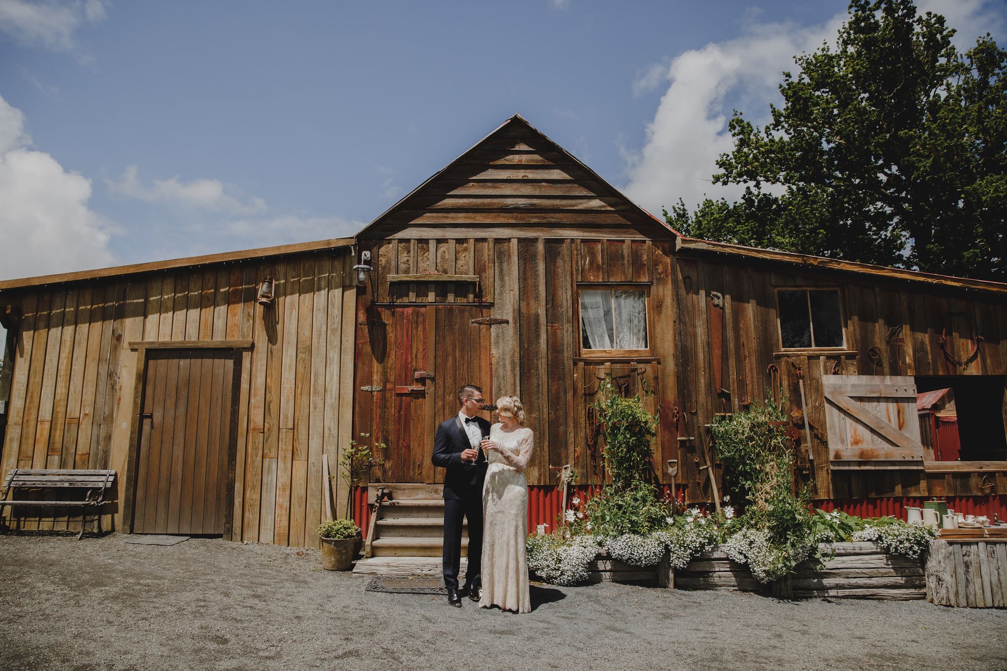 Weathered timber barn with vertical board cladding, a sliding barn door and a planted front border under a blue sky