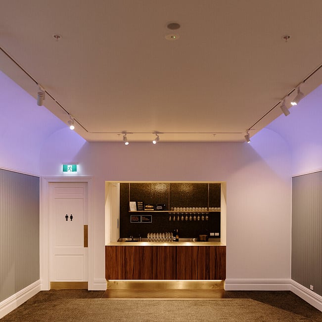 White-painted room with coloured uplighting and a built-in bar alcove with dark tiled splashback