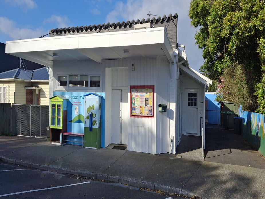 Small white weatherboard community building with covered entrance and notice board