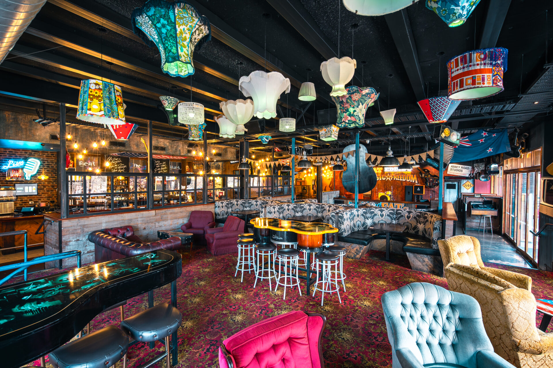 Colourful bar lounge with patterned carpet, mismatched lampshades, velvet chairs and decorative instruments