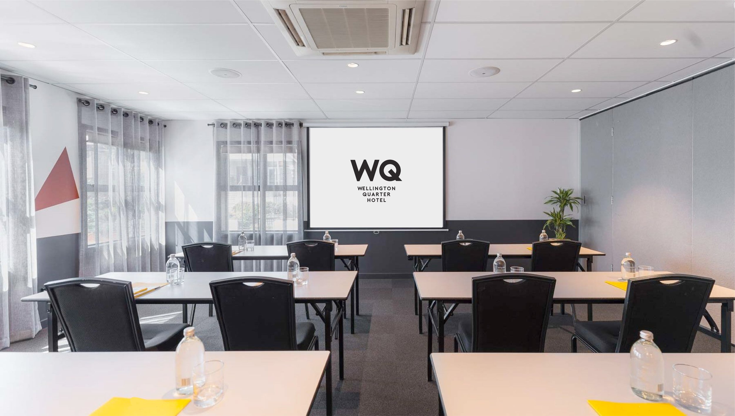 White-walled meeting room with black chairs, white tables, projection screen, and coloured wall feature