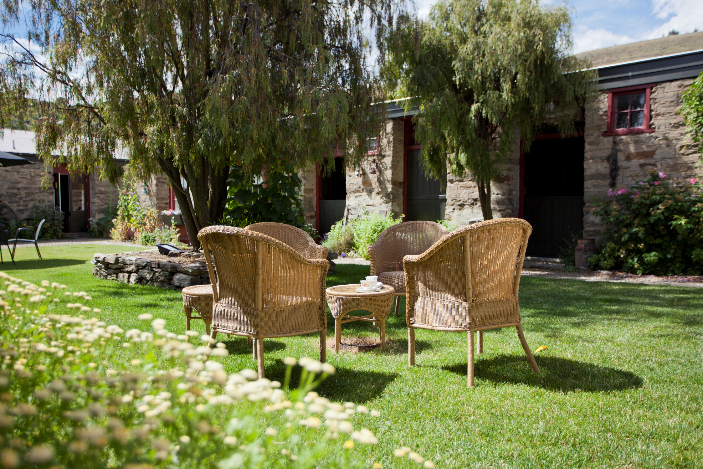 Sunny courtyard with wicker chairs on a lawn and historic schist-stone buildings with red window frames