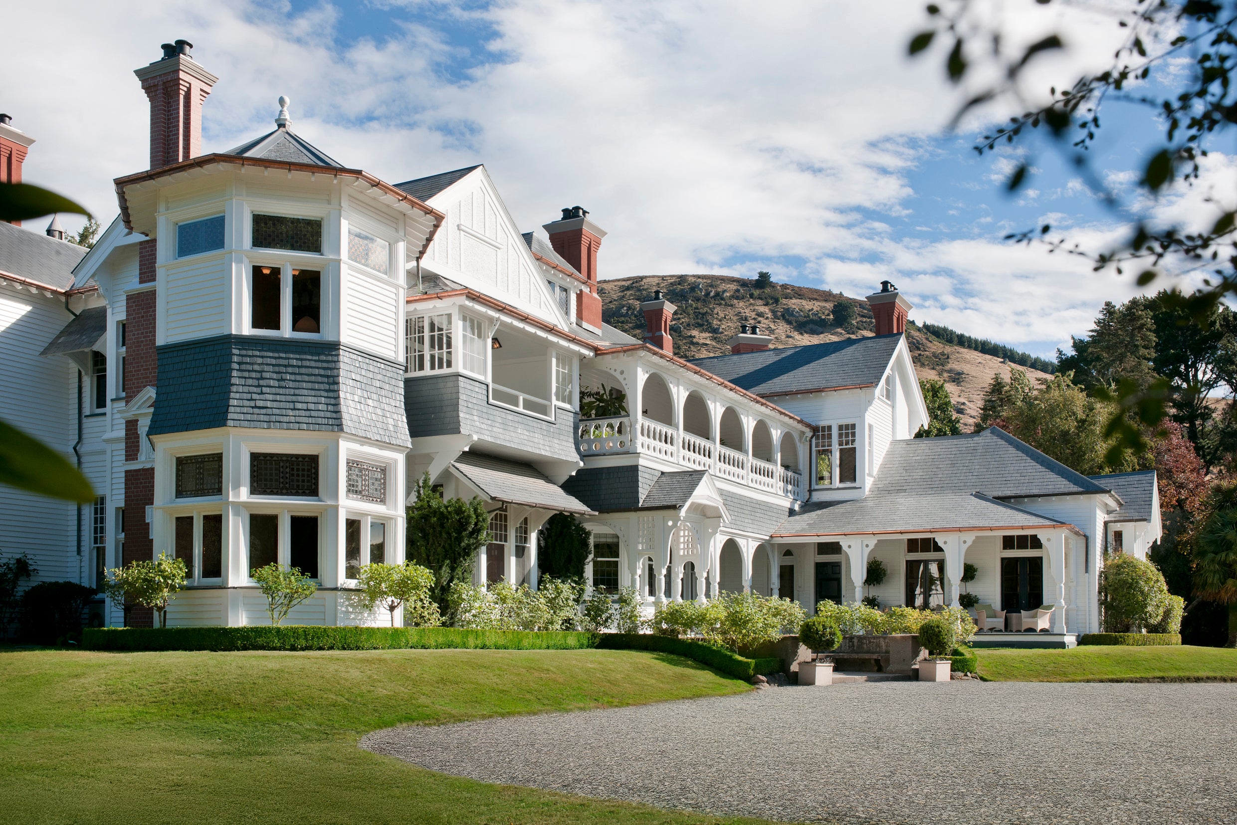 Large Victorian timber mansion with bay tower, wraparound veranda, slate roof, and manicured lawn and gravel drive