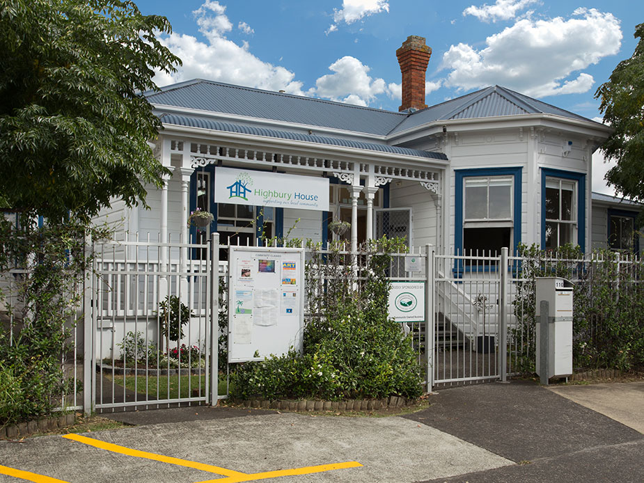 White weatherboard villa exterior with decorative veranda, metal fence, and street frontage